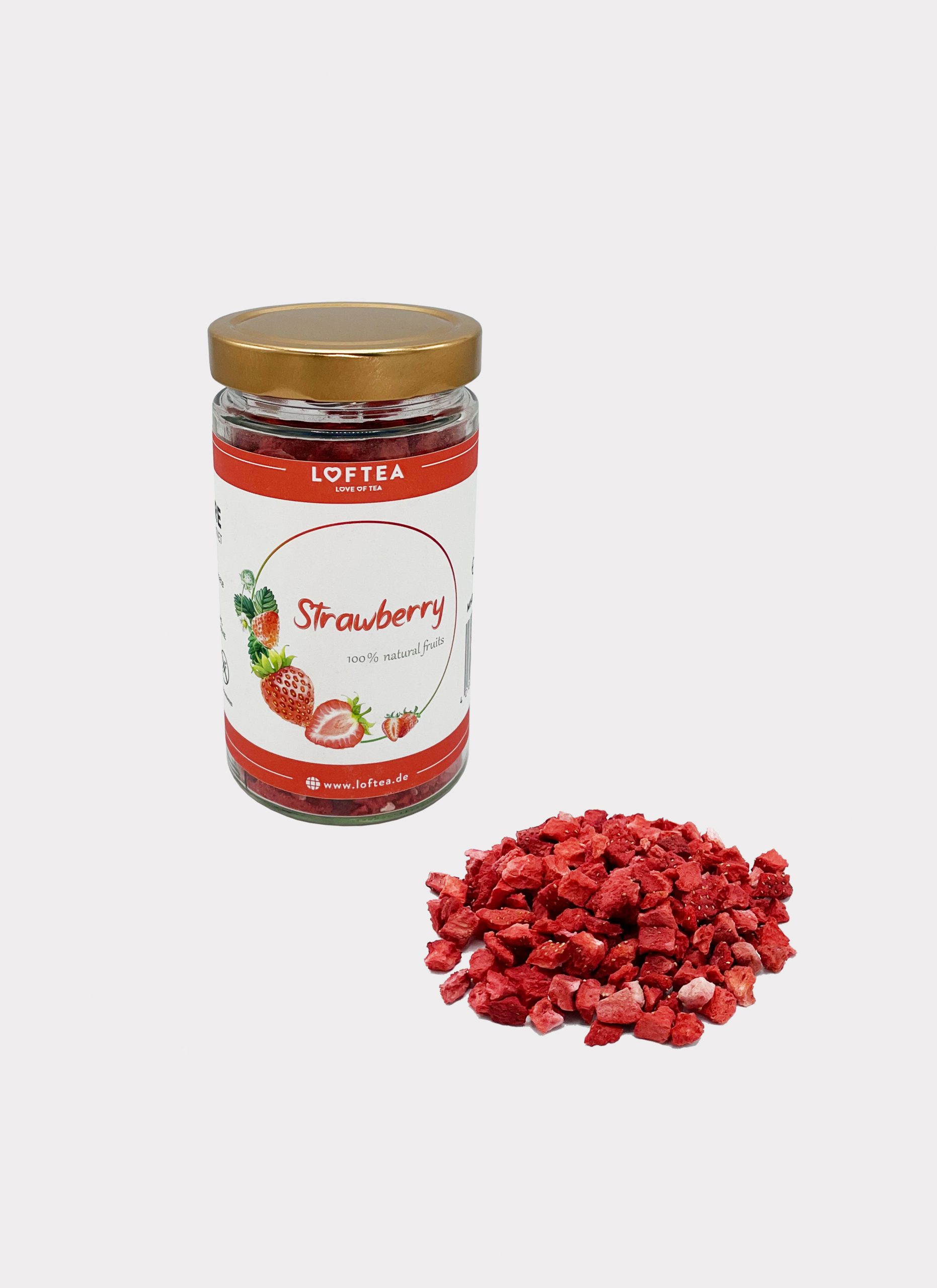 Ein Glas mit gefriergetrockneten Erdbeeren und einem goldenen Deckel steht neben einem kleinen Haufen getrockneter Erdbeerstücke. Das Etikett zeigt Erdbeeren und grüne Blätter auf weißem Hintergrund.