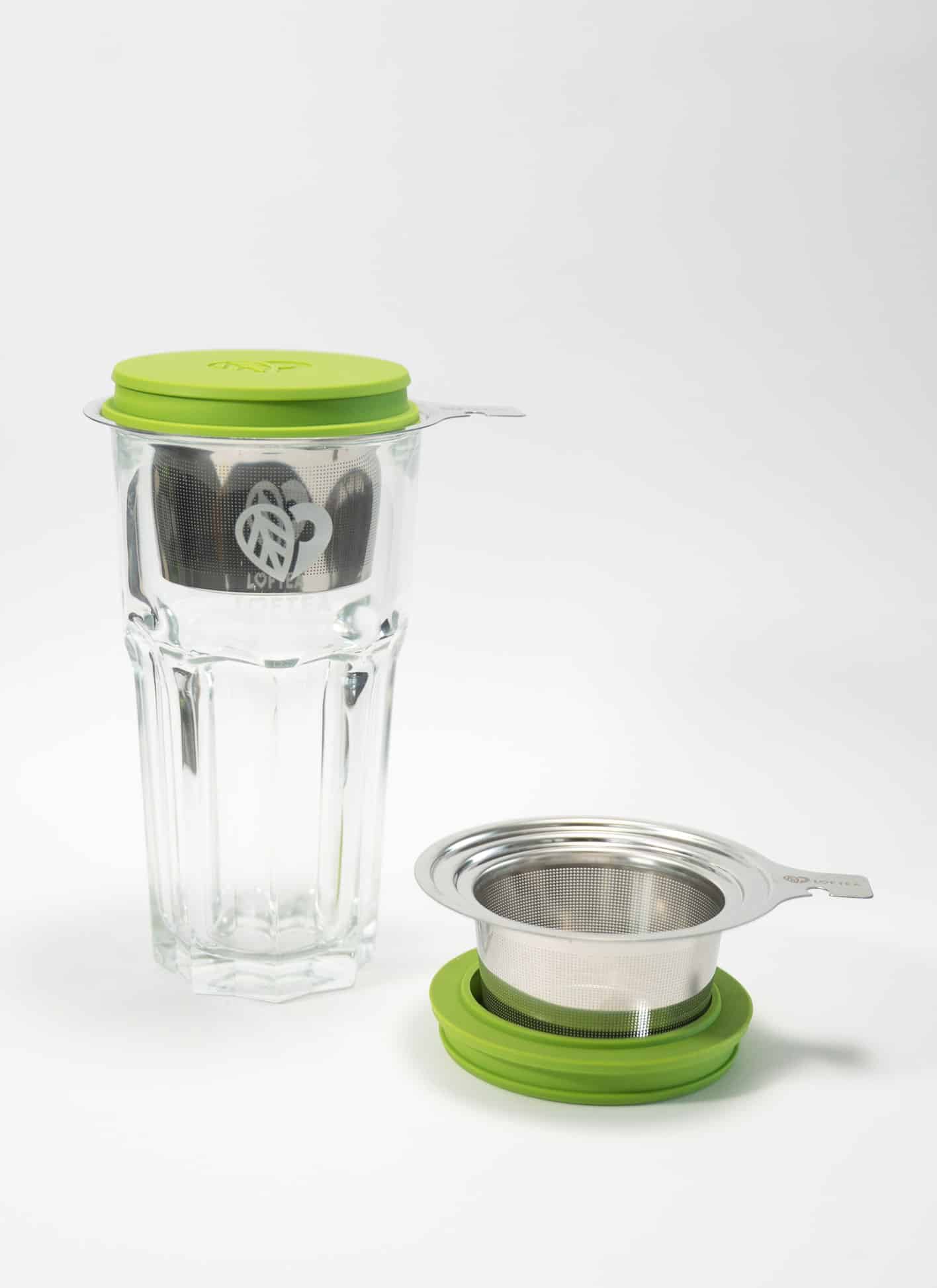 Das LOFTEA – ICE BREW Tee-Set mit grünem Deckel enthält ein Teesieb aus Glas mit Edelstahlsieb, Griff und passendem grünen Unterteil. Das florale Logo ziert das Glas elegant und unterstreicht das ruhige Ambiente vor einem strahlend weißen Hintergrund.