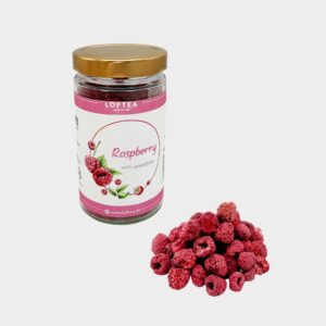 Das Glas „Raw – gefriergetrocknete Himbeeren“ mit seinem goldenen Deckel steht neben einem kleinen Haufen gefriergetrockneter Himbeeren auf einem weißen Hintergrund und weist ein Himbeerbild und eine detaillierte Markenbezeichnung auf dem Etikett auf.