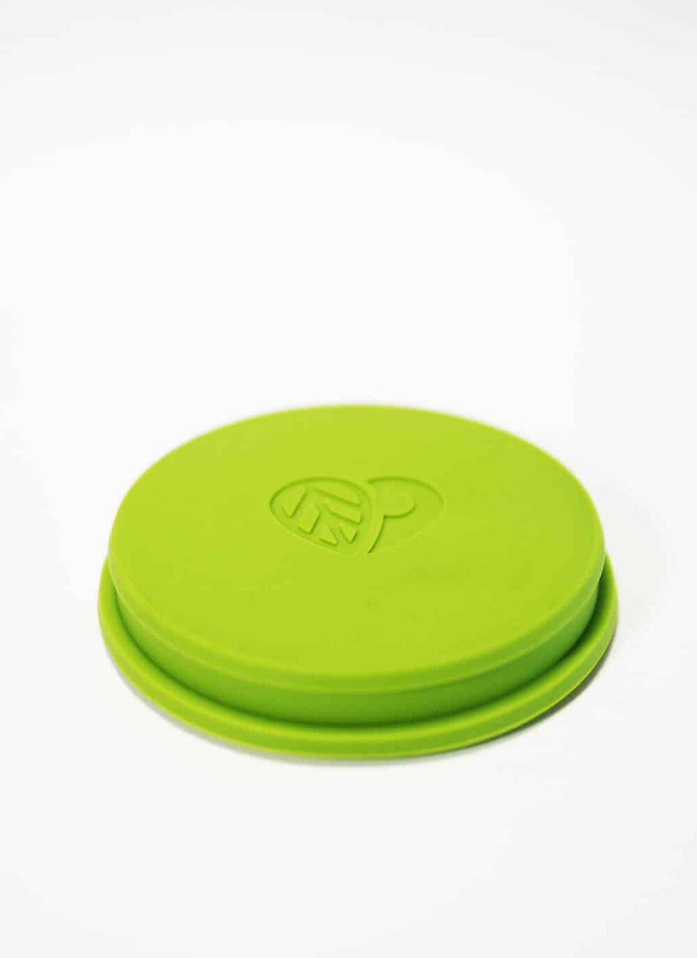 Ein runder, grüner Silikondeckel mit einem erhabenen Herz- und Blattdesign in der Mitte, das an das entzückende LOFTEA – ICE BREW Tee-Set inkl. 200 g Tee nach Wahl erinnert, vor einem schlichten weißen Hintergrund.