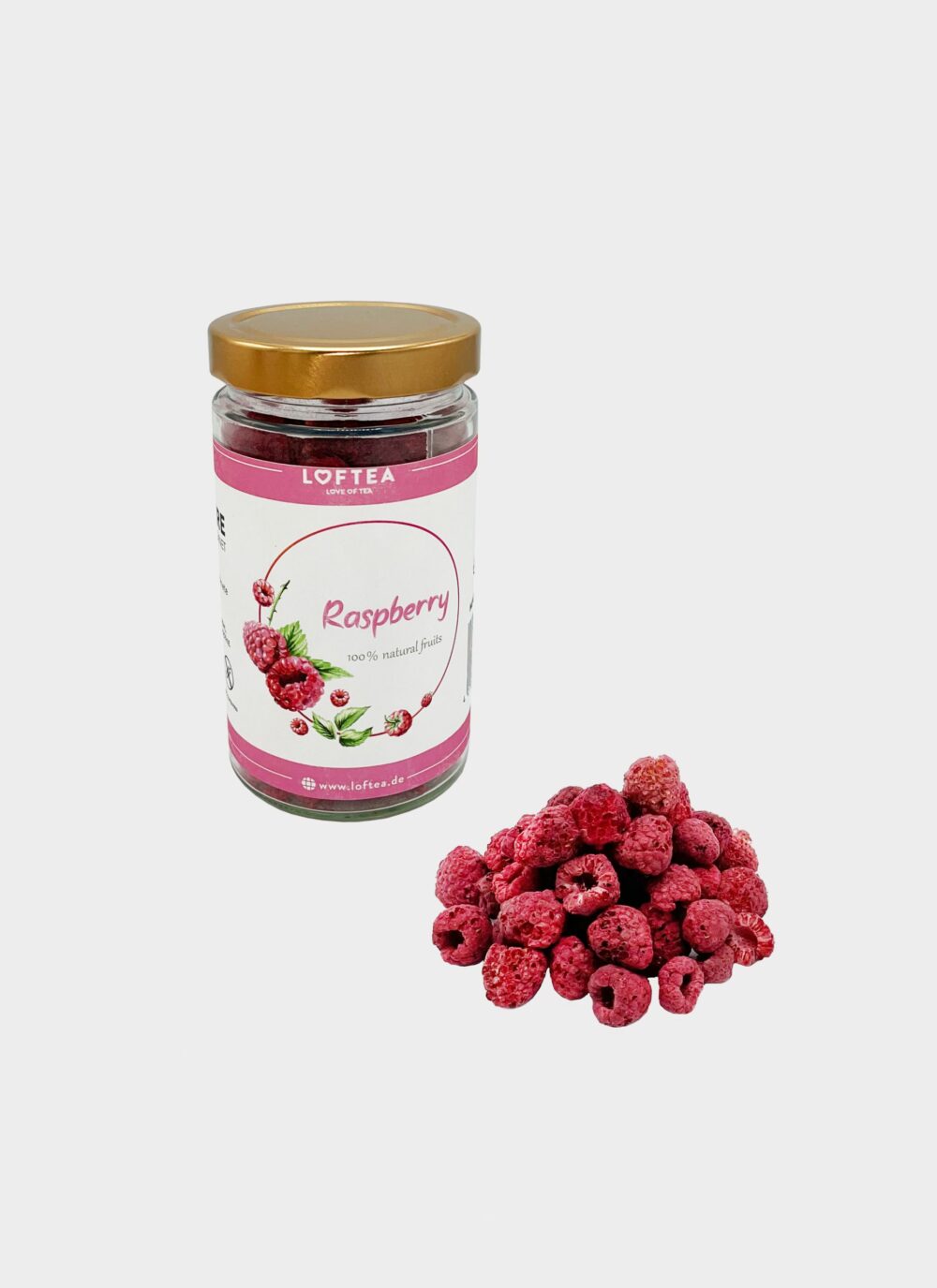 Das Glas „Raw – gefriergetrocknete Himbeeren“ mit seinem goldenen Deckel steht neben einem kleinen Haufen gefriergetrockneter Himbeeren auf einem weißen Hintergrund und weist ein Himbeerbild und eine detaillierte Markenbezeichnung auf dem Etikett auf.