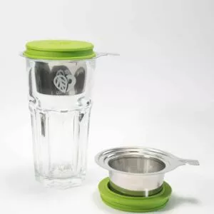 Das LOFTEA – ICE BREW Tee-Set mit grünem Deckel enthält ein Teesieb aus Glas mit Edelstahlsieb, Griff und passendem grünen Unterteil. Das florale Logo ziert das Glas elegant und unterstreicht das ruhige Ambiente vor einem strahlend weißen Hintergrund.