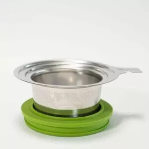 Der LOFTEA Siebträger + Deckel ist ein Tee-Ei aus Edelstahl mit einem feinmaschigen Sieb, das perfekt in einen grünen Silikonhalter passt. Er verfügt über einen schlanken Deckel und einen kleinen Griff an einer Seite für eine einfache Handhabung, während sein minimalistisches und funktionales Design seinen modernen Reiz unterstreicht.