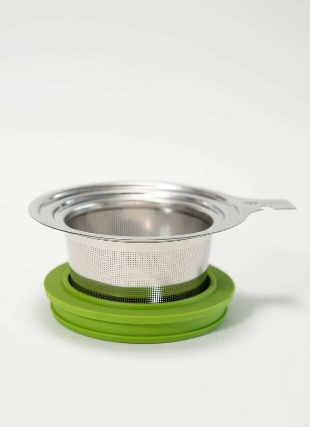 Das LOFTEA – ICE BREW Tee-Set enthält ein Teesieb aus Edelstahlgeflecht mit einer grünen Silikonbasis, die das Set perfekt ergänzt. Es verfügt über einen praktischen Griff zum einfachen Herausnehmen und präsentiert sich elegant vor einem schlichten weißen Hintergrund.