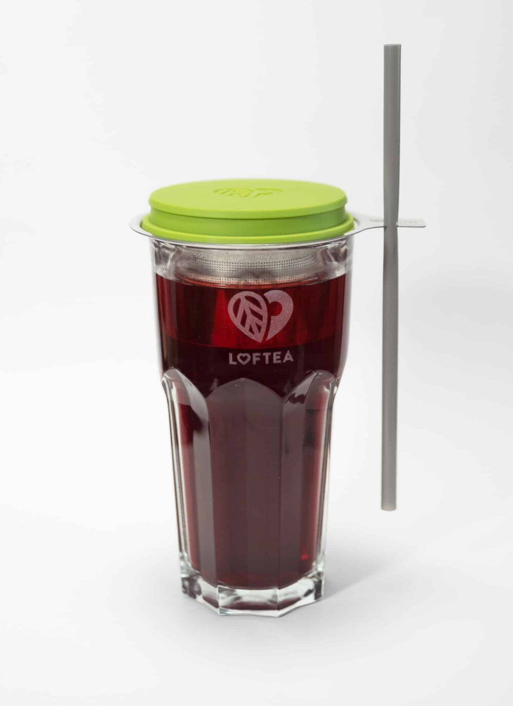 Ein hohes Glas mit dunkelroter Flüssigkeit, verziert mit einem herzförmigen LOFTEA-Logo, präsentiert einen grünen Deckel und einen Metallstrohhalm. Dieses exquisite LOFTEA – ICE BREW Tee-Set inkl. 200g Tee nach Wahl ist ideal für alle, die bei ihrem Teegenuss Wert auf Qualität und Stil legen.